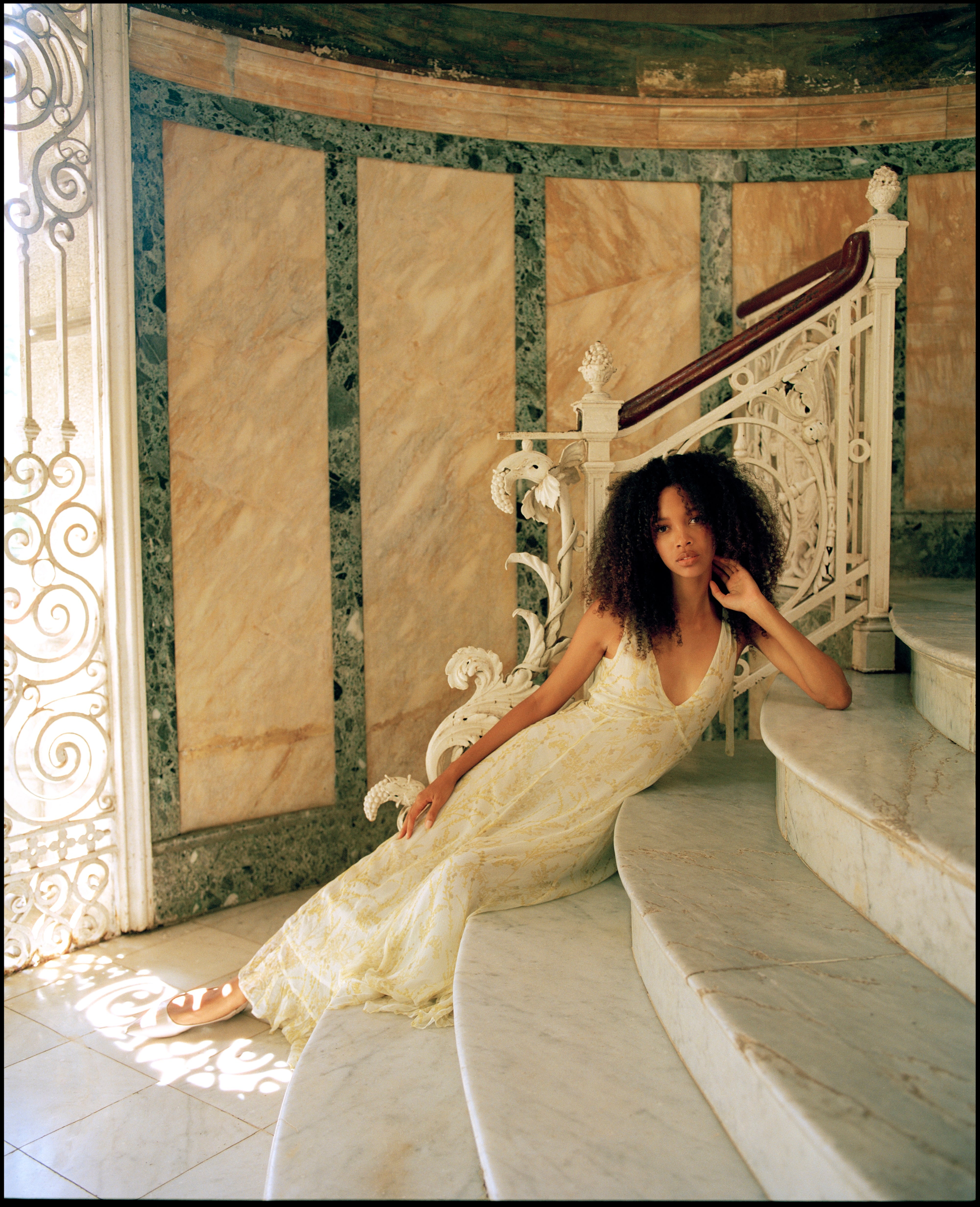 Woman in a yellow dress sitting on a marble staircase with ornate railings.