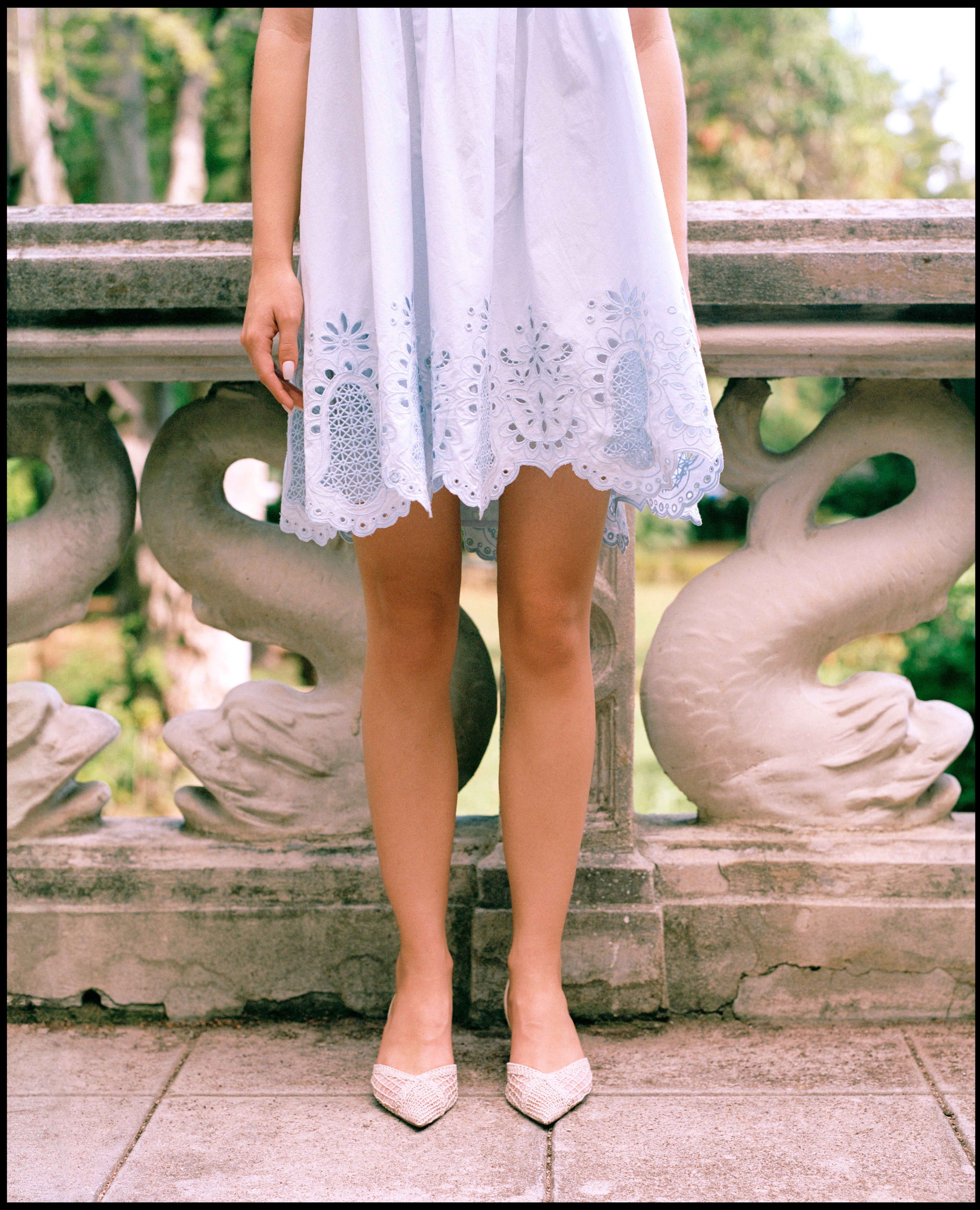Person wearing a white lace dress standing on a stone bridge.